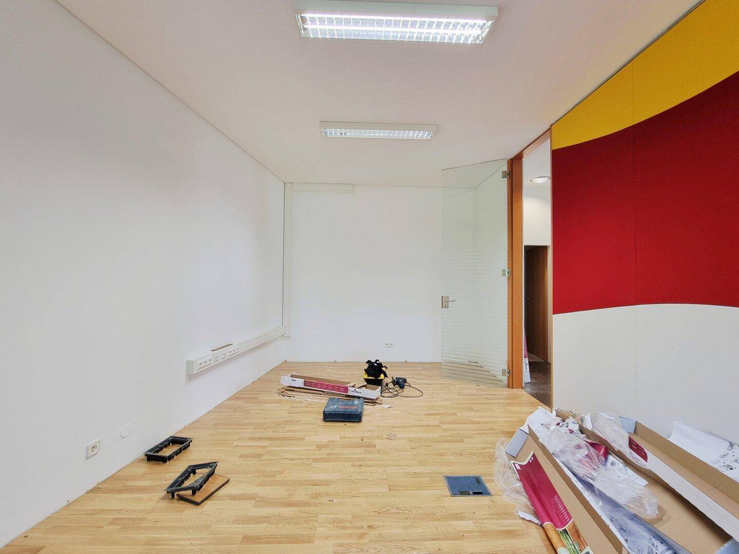 Leerer Raum mit Holzboden und Glaswand, ideal für ein modernes Büro oder Geschäft.