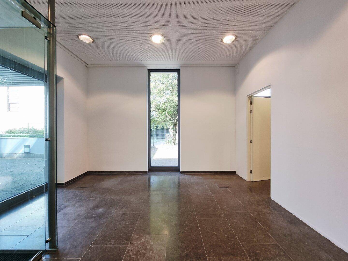 Heller Raum mit Fliesenboden und hohem Fenster, das viel Tageslicht hereinlässt.