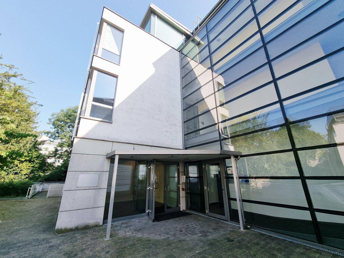 Moderne Gebäudefassade mit großen Glasflächen und klaren Linien unter blauem Himmel.