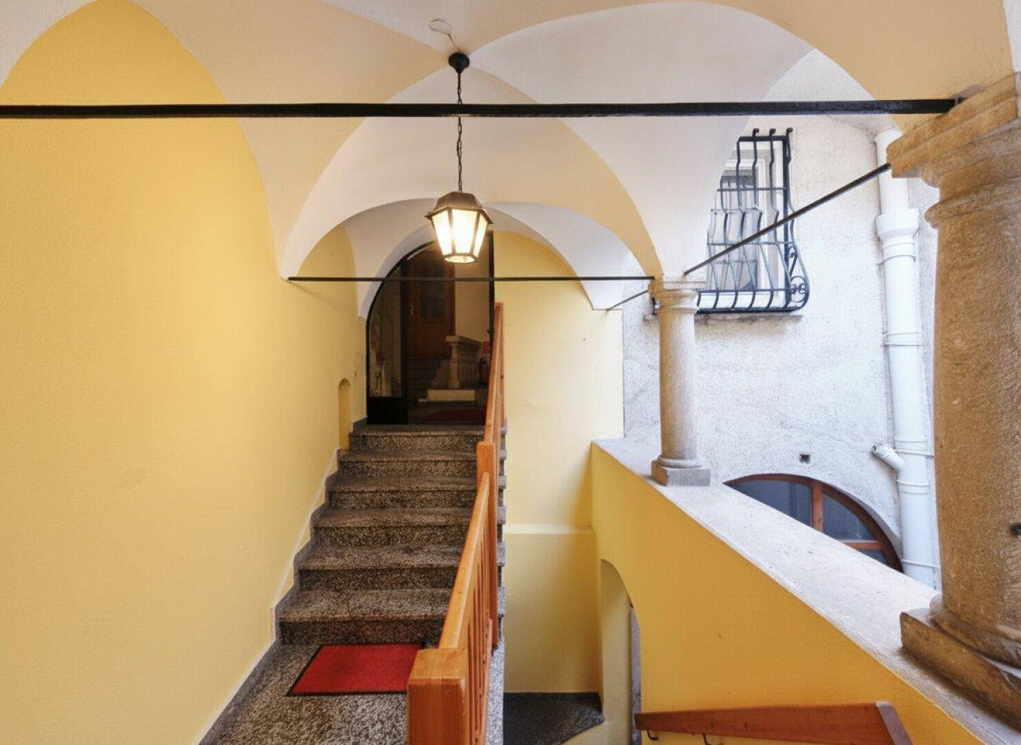 Historisches Treppenhaus mit Gewölbedecke, Steinstufen und Holzgeländer in einem Altbau.