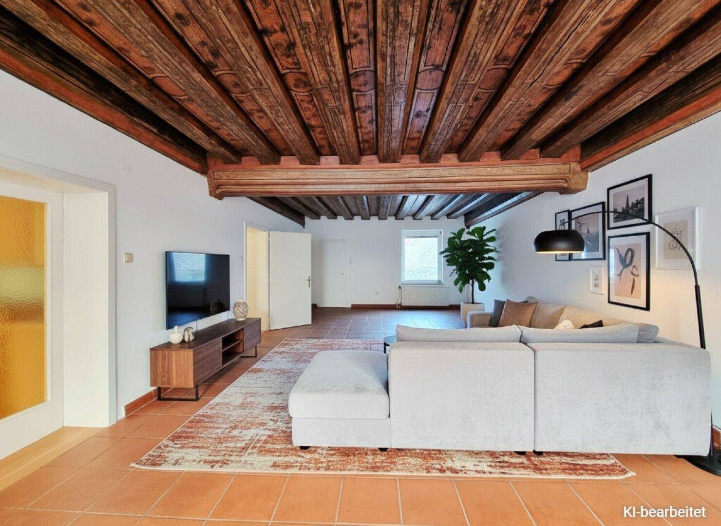 Geräumiges Wohnzimmer mit freiliegenden Holzbalken an der Decke und Terrakottaboden.
