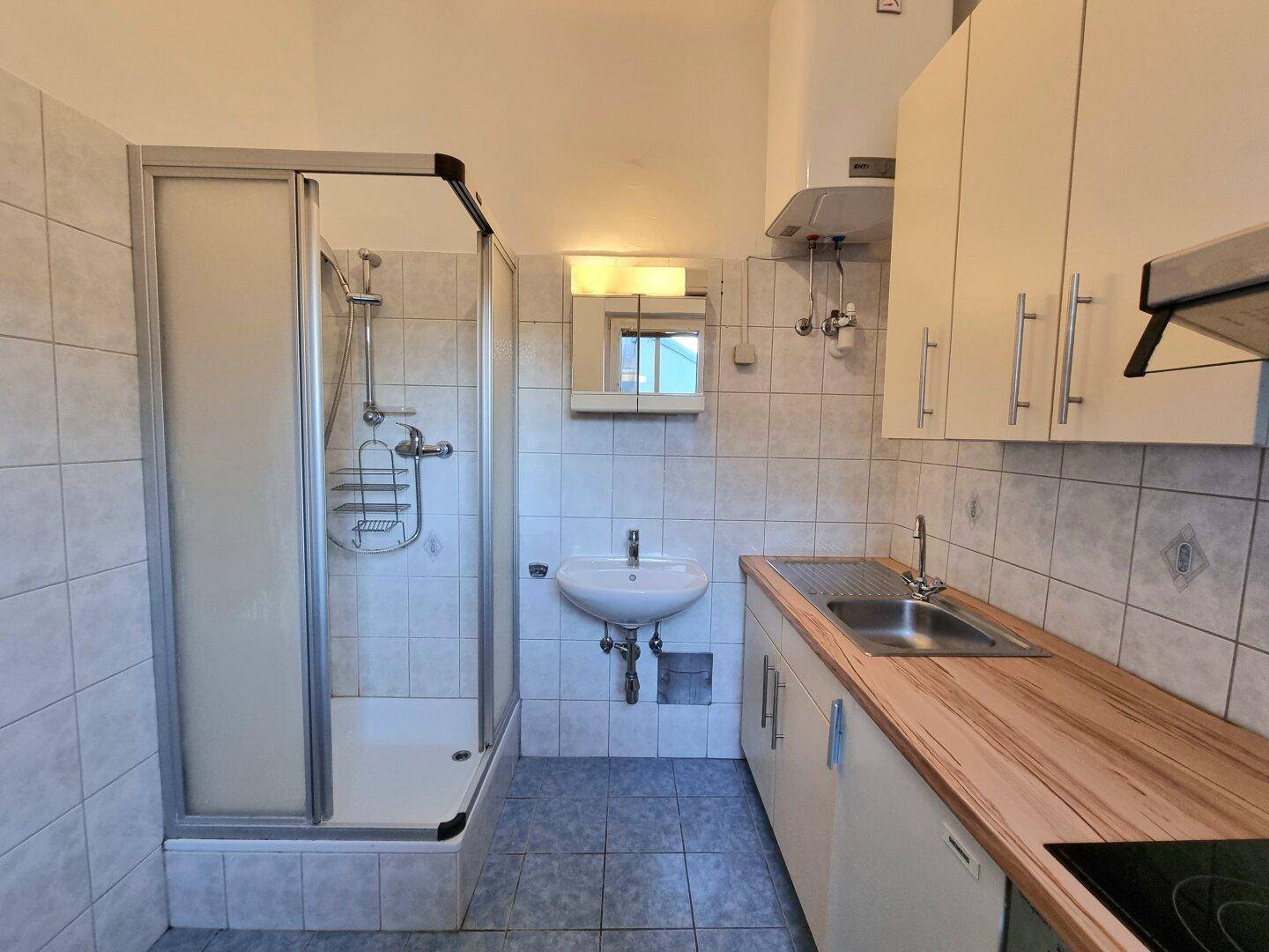 Kleines Badezimmer mit Dusche, Waschbecken und integrierter Küchenzeile.
