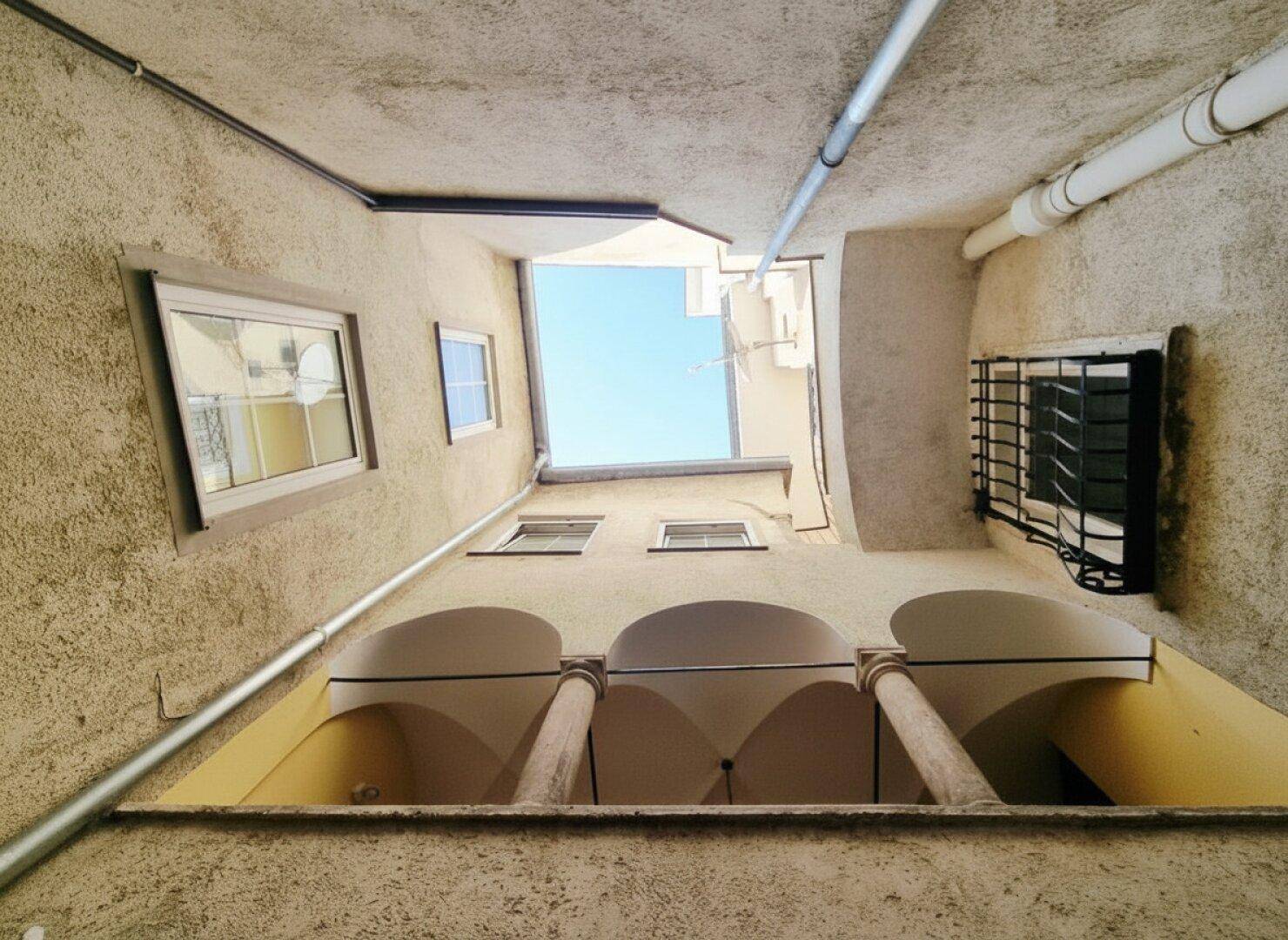 Blick nach oben in einen engen Innenhof mit historischen Fenstern und Säulen.