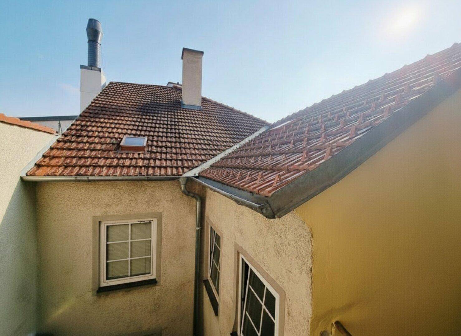 Blick auf die Dächer eines Altbaus mit Ziegeln und Schornsteinen unter blauem Himmel.