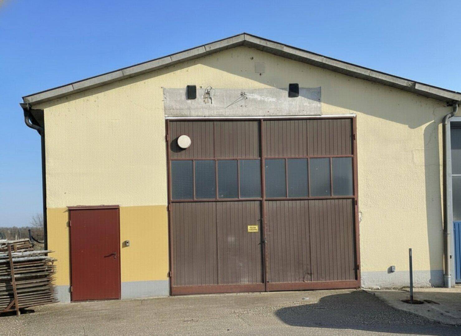 Außenansicht eines Industriegebäudes mit gelber Fassade, großem braunem Tor und Satteldach.