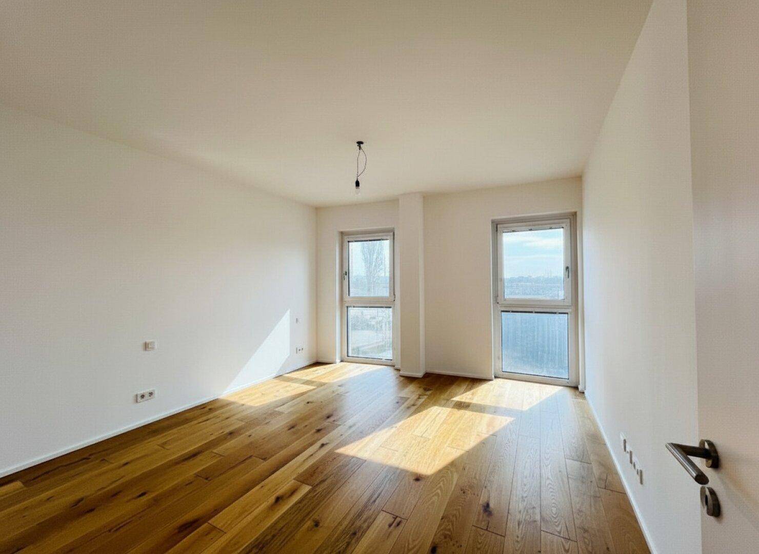 Heller, leerer Raum mit Holzdielenboden und Zugang zu einem potenziellen Balkon.