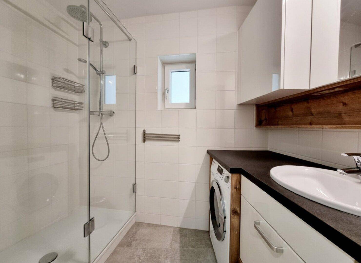 Modernes Badezimmer mit begehbarer Dusche, Waschmaschine und Fenster für Tageslicht.