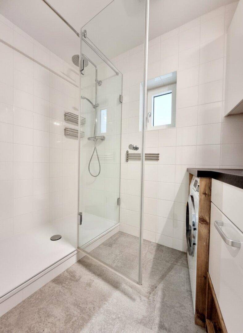 Helles Badezimmer mit geräumiger begehbarer Dusche und integrierter Waschmaschine.