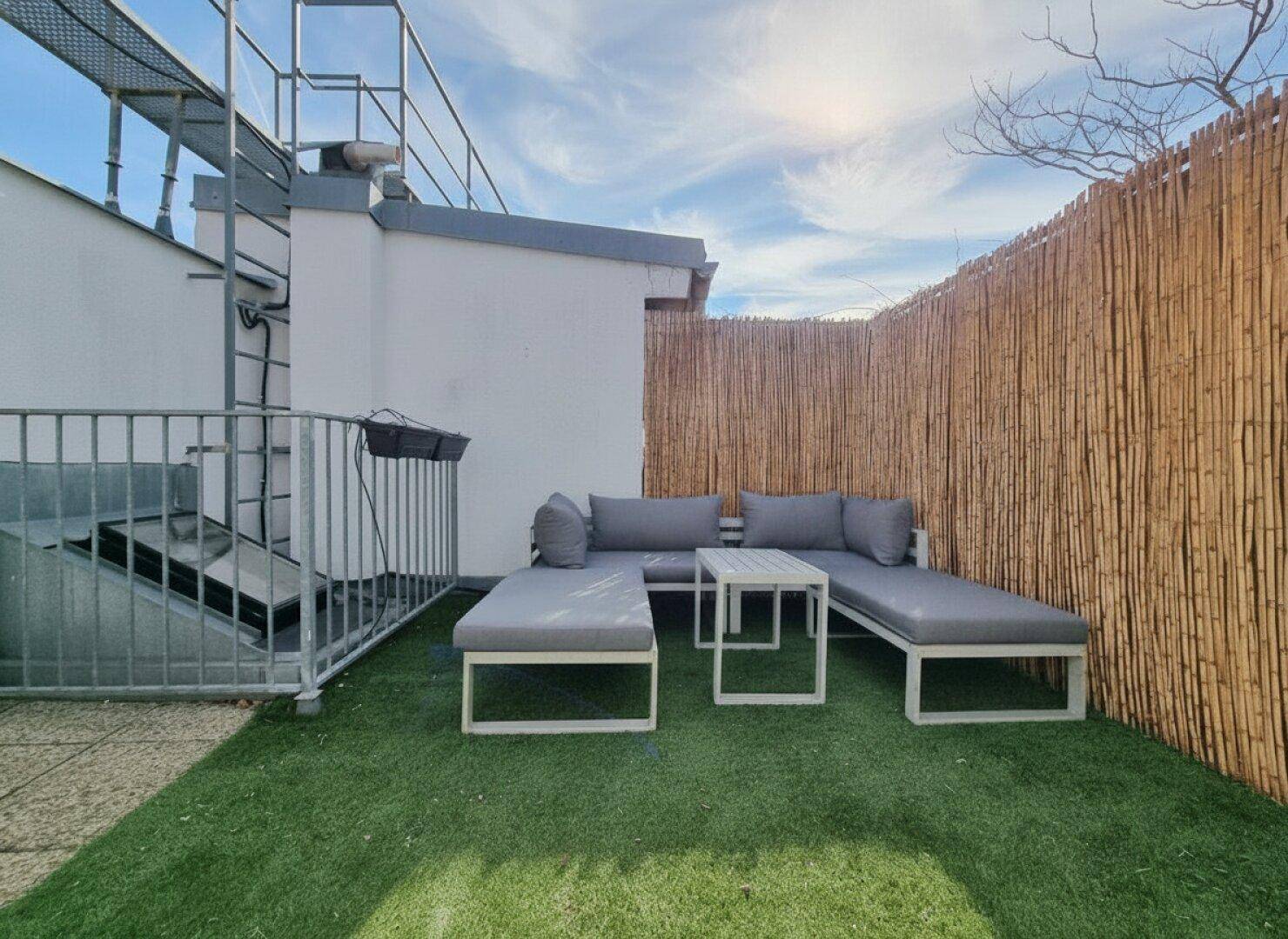 Gemütliche Dachterrasse mit Kunstrasen, Loungemöbeln und Sichtschutz aus Bambus.