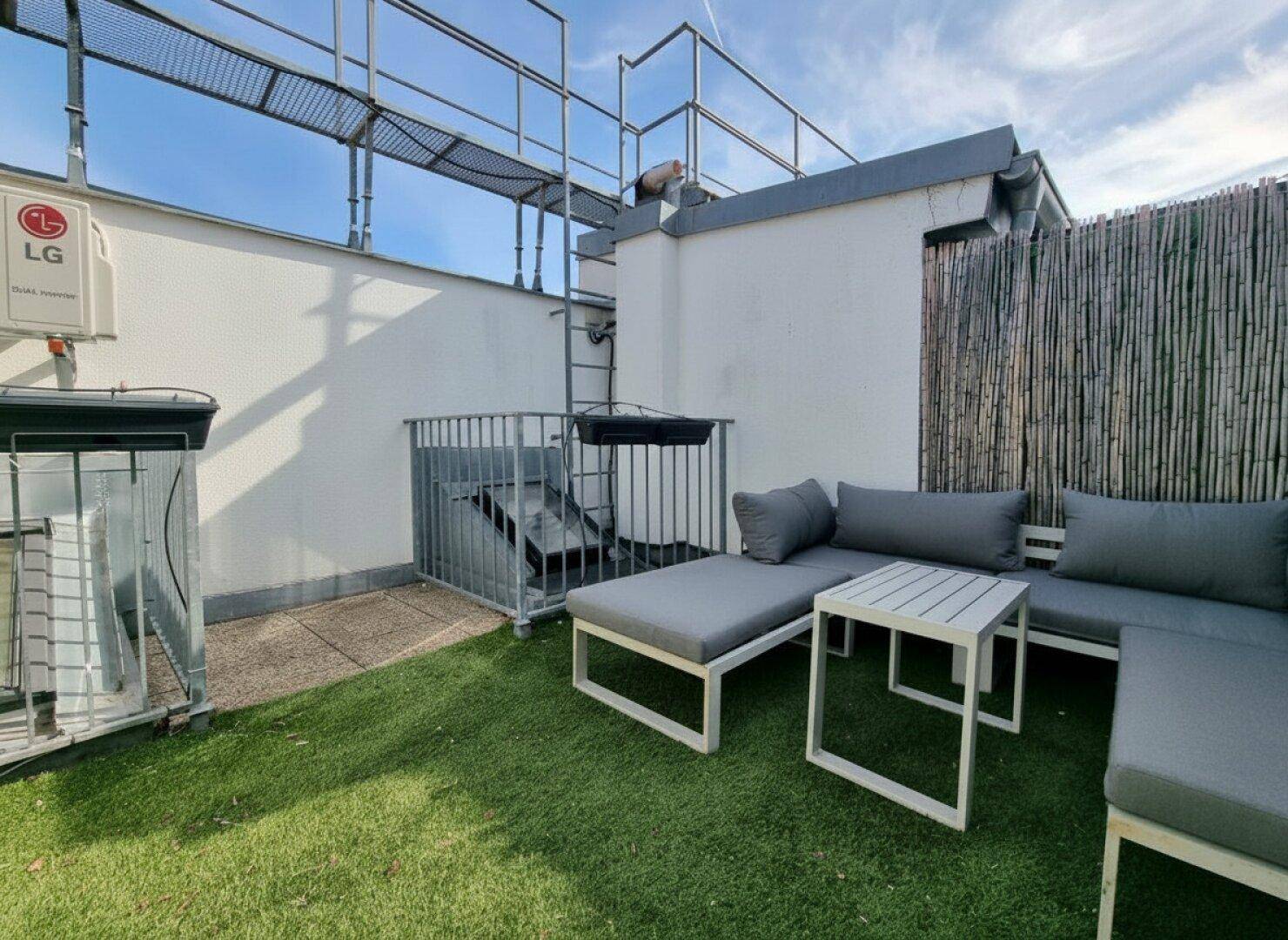 Dachterrasse mit Kunstrasen, bequemen Loungemöbeln und Klimaanlage im Freien.