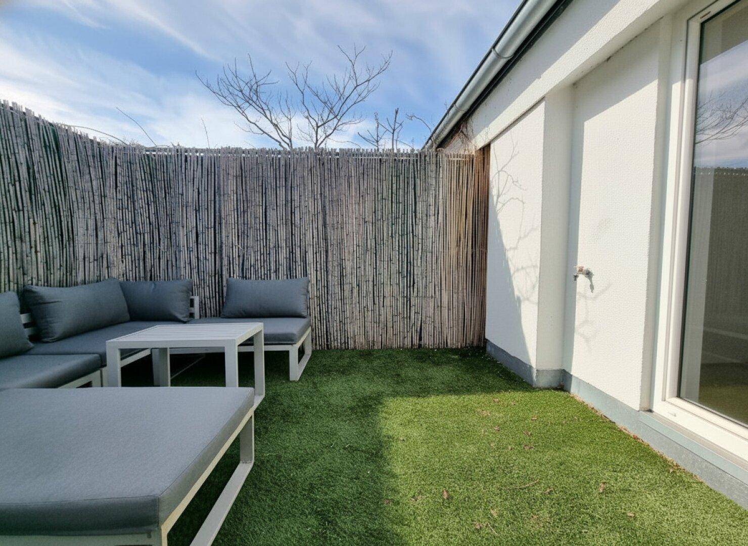 Ruhige Dachterrasse mit Kunstrasen, Loungemöbeln und natürlichem Sichtschutz.