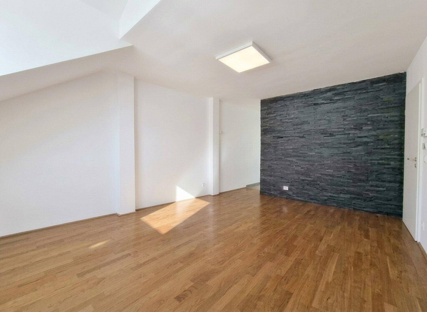 Geräumiger Wohnbereich mit dunkler Steinwand als Akzent und hellem Holzfußboden.