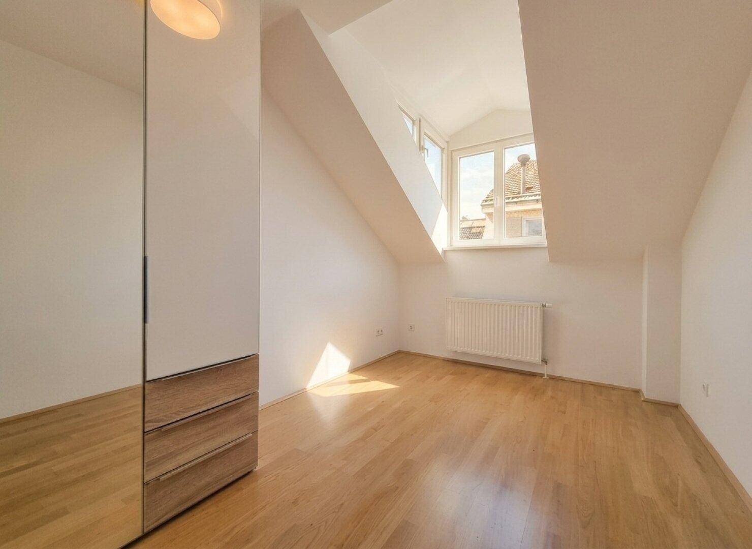 Helles Schlafzimmer im Dachgeschoss mit Holzfußboden, Schrägen und Spiegelschrank.