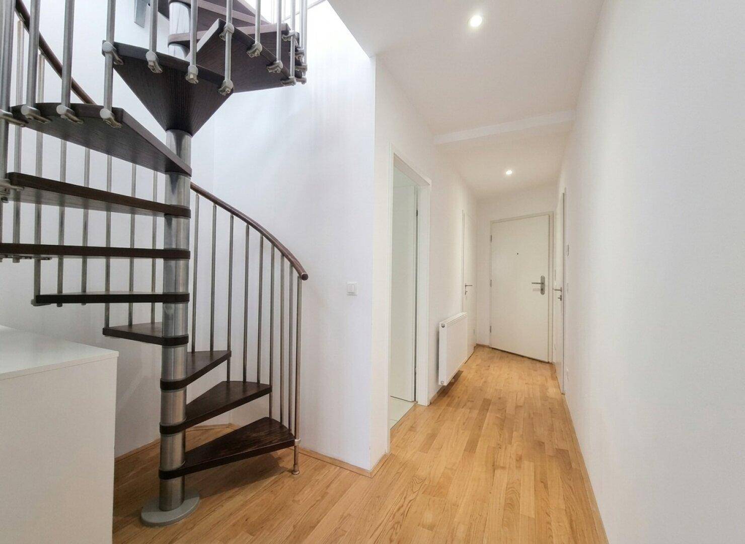 Heller Flur mit eleganter Wendeltreppe, Holzfußboden und weißen Wänden.