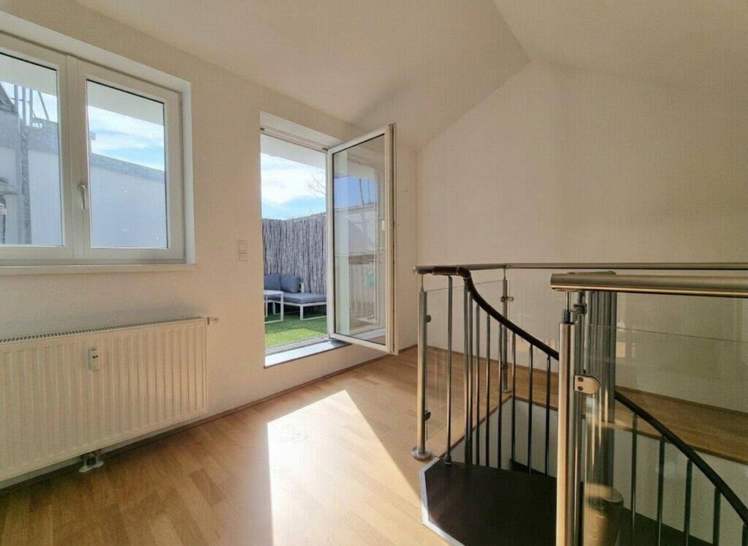 Heller Treppenaufgang mit Zugang zu einem kleinen Außenbereich mit Sitzgelegenheiten.