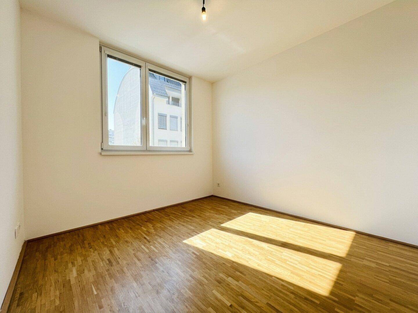 Sonniger Raum mit Parkettboden und weiß gestrichenen Wänden, ideal als Schlaf- oder Arbeitszimmer.