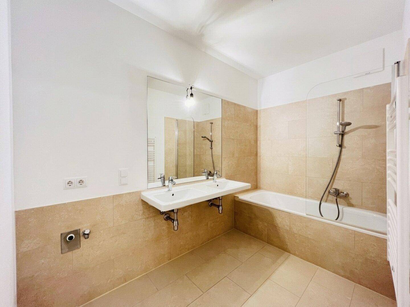 Modernes Badezimmer mit beigen Fliesen, Doppelwaschbecken und Badewanne mit Duschfunktion.