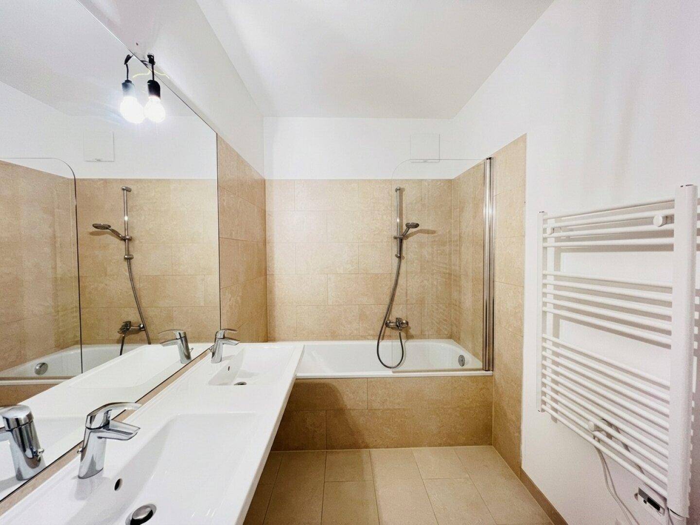 Geräumiges Badezimmer mit beigen Wand- und Bodenfliesen, Doppelwaschbecken und Badewanne.