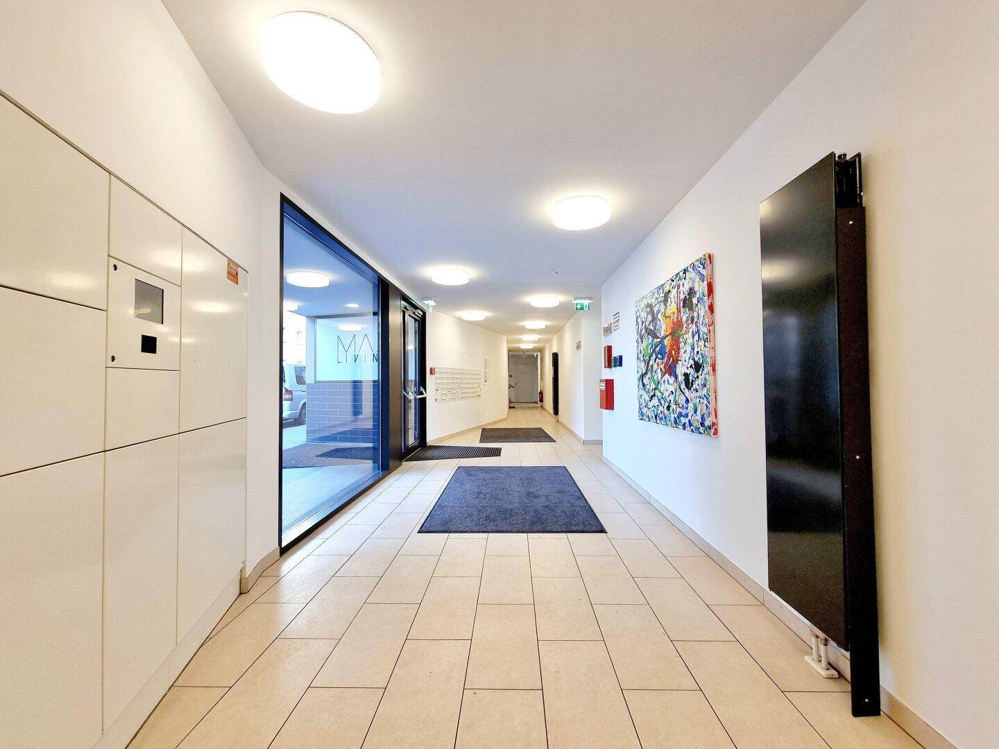 Moderner Eingangsbereich mit Fliesenboden, Paketboxen und heller Beleuchtung in einem Mehrfamilienhaus.