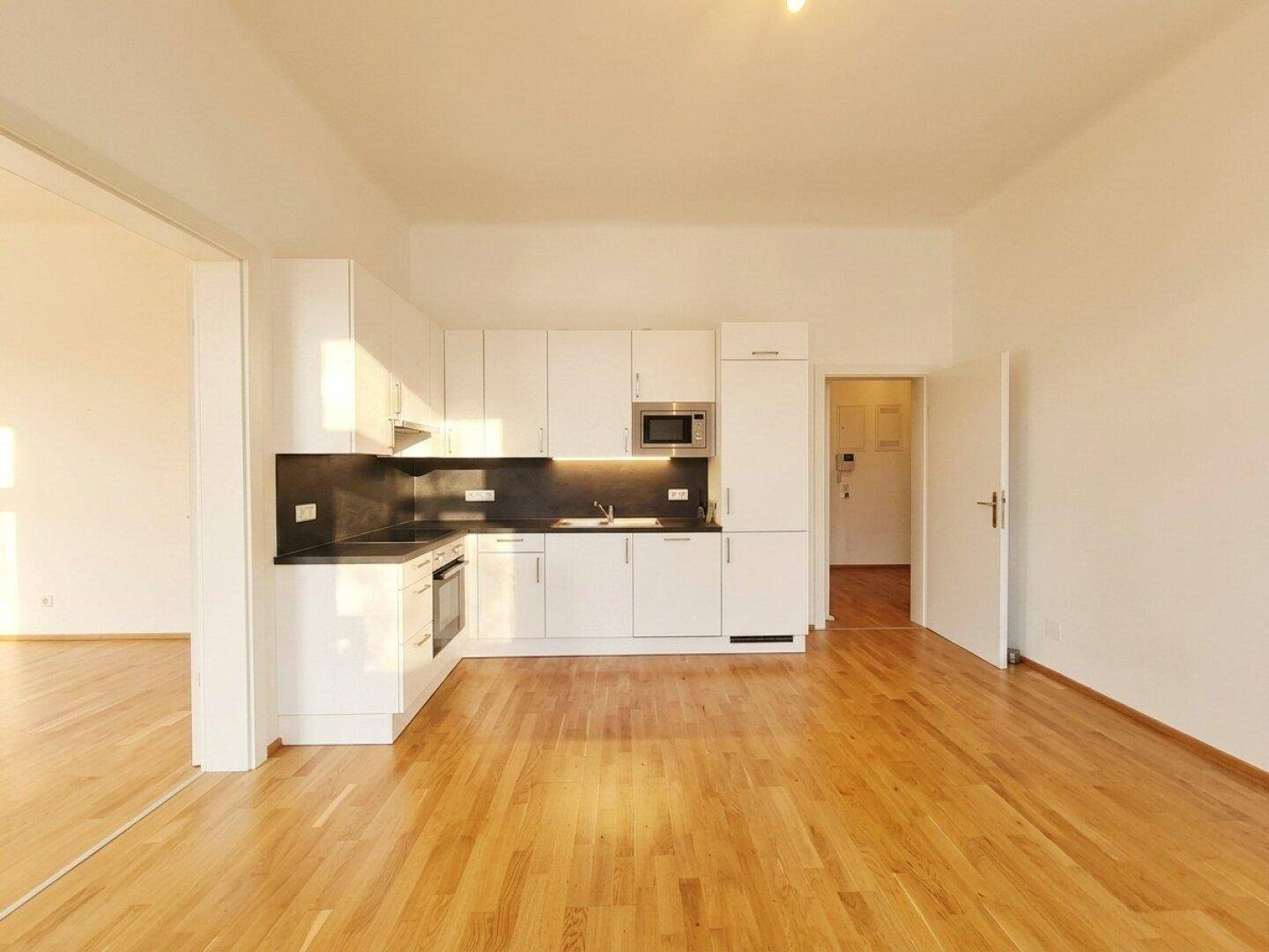 Moderne Einbauküche in Weiß mit integrierten Geräten und Zugang zu einem weiteren Zimmer.