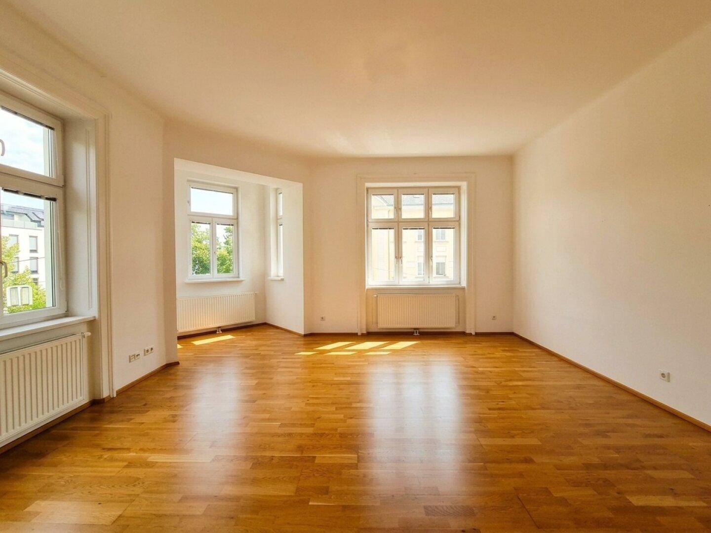 Lichtdurchfluteter Raum mit Holzboden und mehreren Fenstern, ideal für Wohn- oder Schlafbereich.