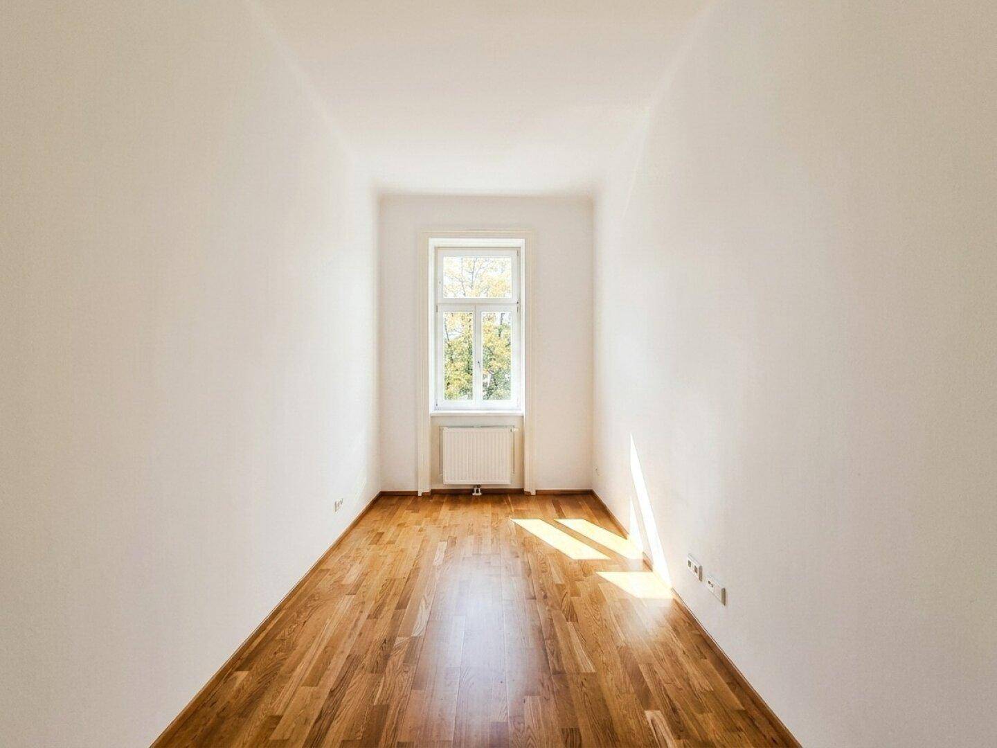 Schmaler, heller Raum mit Parkettboden und einem Fenster, ideal als Kinder- oder Arbeitszimmer.
