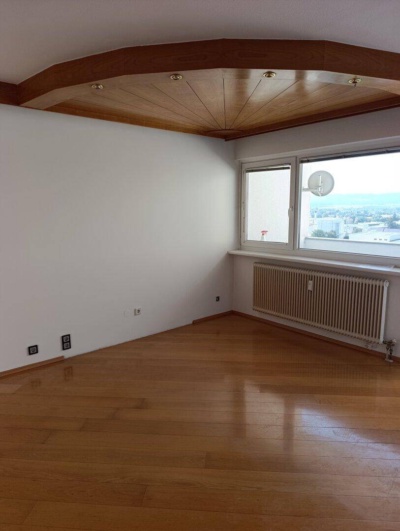 Heller Wohnbereich mit Stadtblick, Parkettboden und dekorativer Holzdecke.
