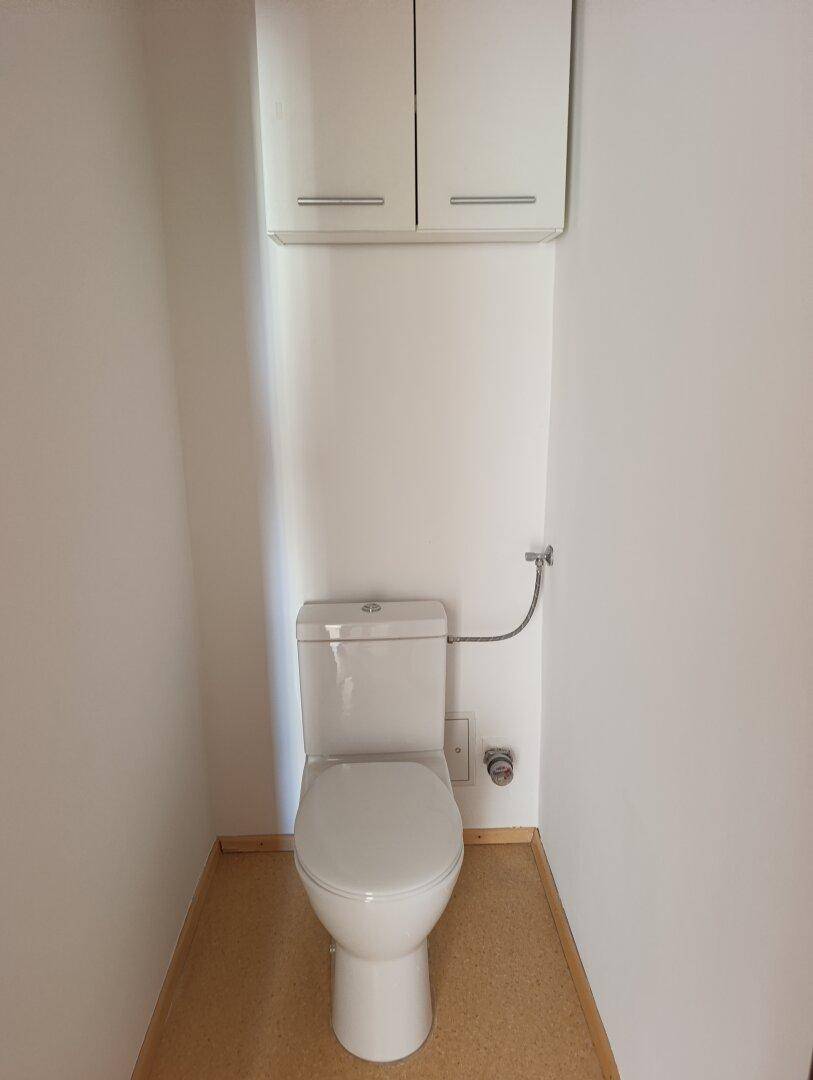 Separates WC mit Toilette und kleinem Wandschrank.