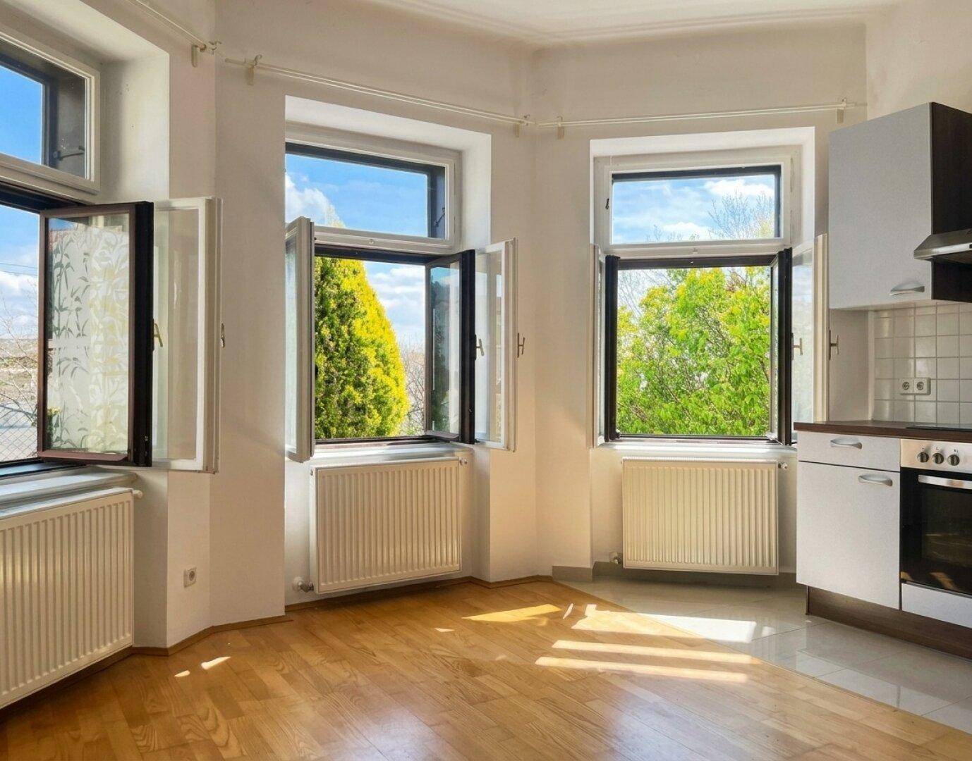 Lichtdurchfluteter Wohnbereich mit offener Küche und Blick ins Grüne durch geöffnete Fenster.