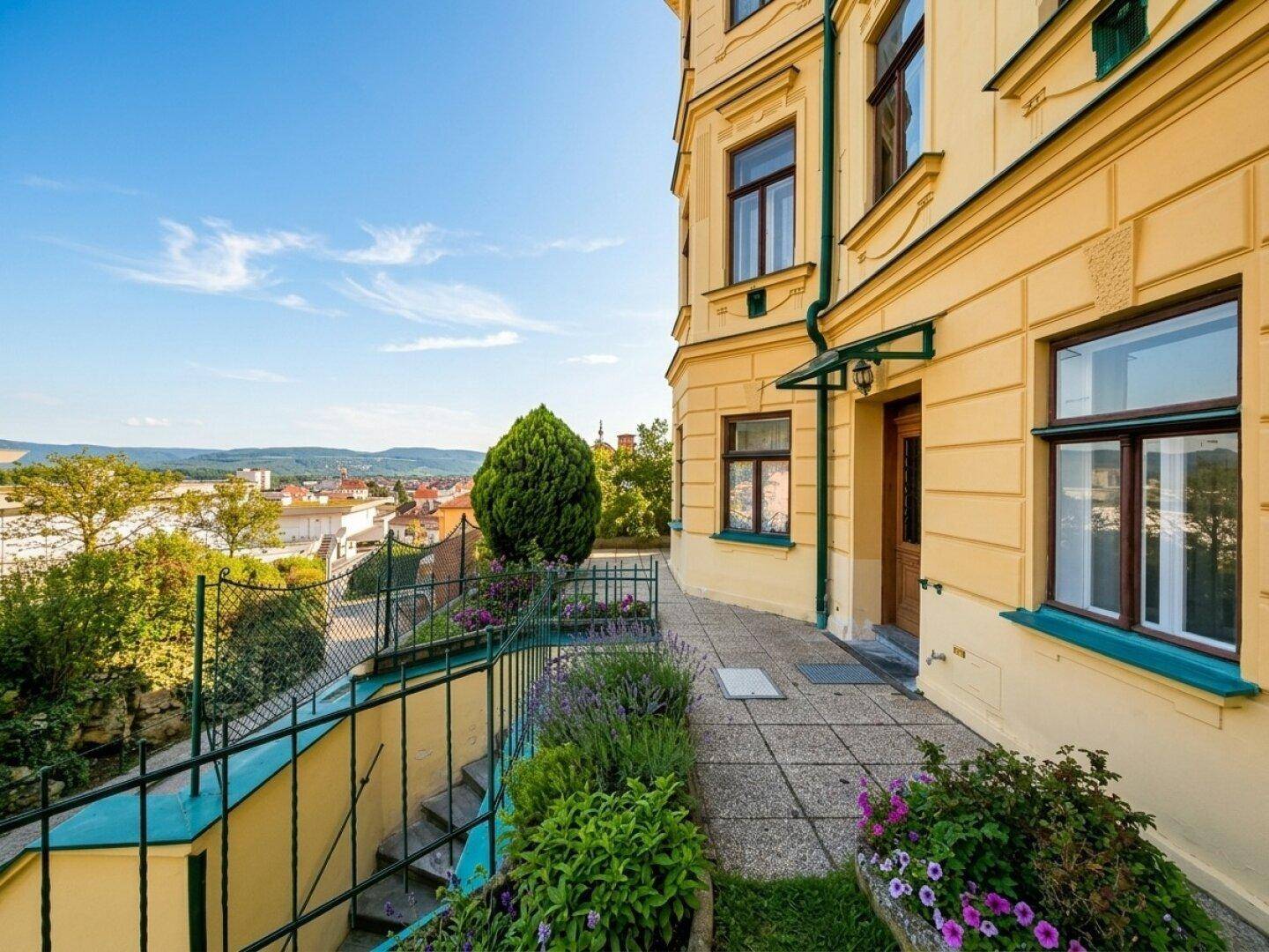Historische Fassade eines Gebäudes mit gepflastertem Weg, Treppe und weitem Blick über die Stadt.