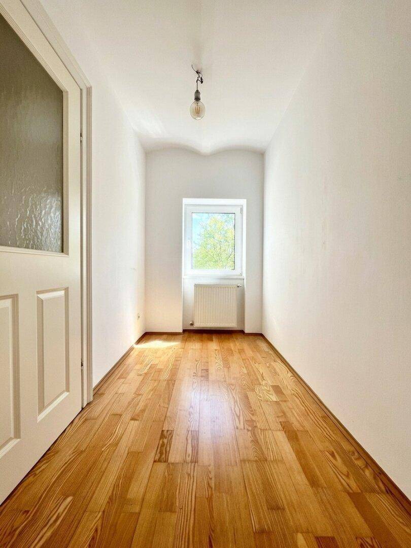Helles Zimmer mit Holzboden, weißen Wänden und einem Fenster, das viel Tageslicht hereinlässt.