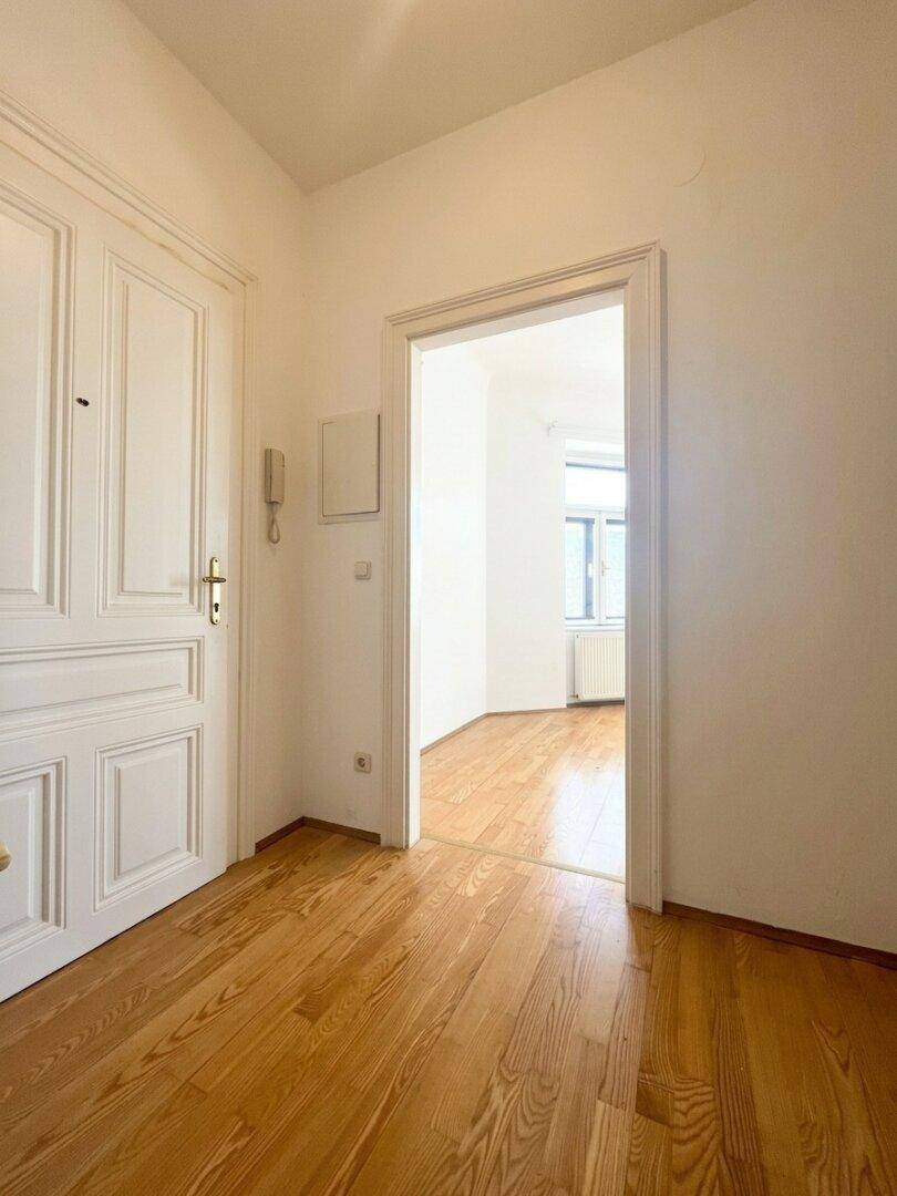 Heller Flur mit Holzboden und einer Gegensprechanlage, der zu einem weiteren Zimmer führt.