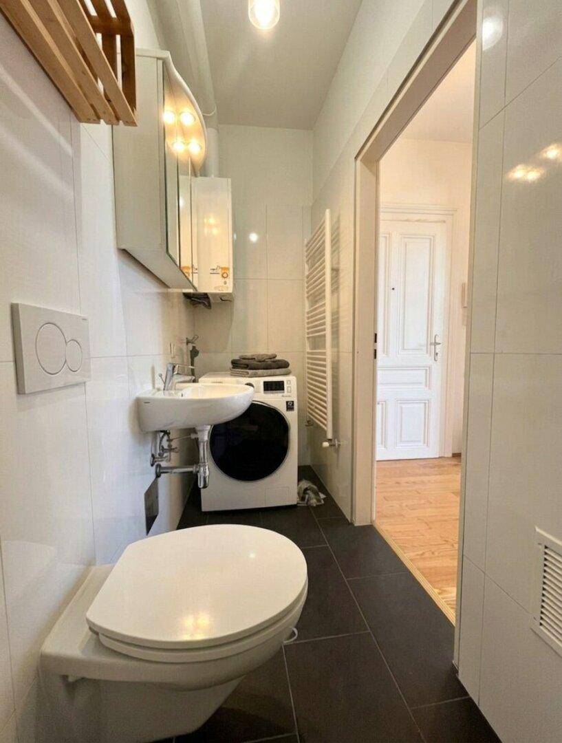 Modernes Badezimmer mit Toilette, Waschbecken, Waschmaschine und beheiztem Handtuchhalter.