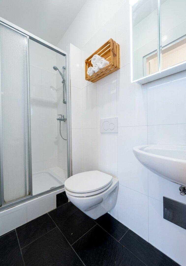 Kompaktes Badezimmer mit Duschkabine, Toilette und Waschbecken, ausgestattet mit modernen Fliesen.