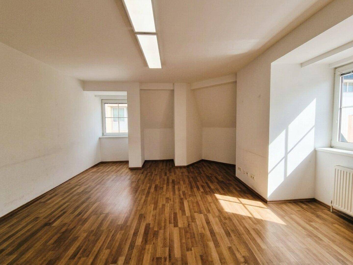 Helles Zimmer mit Laminatboden, weißen Wänden und Nischen, die Stauraum bieten könnten.
