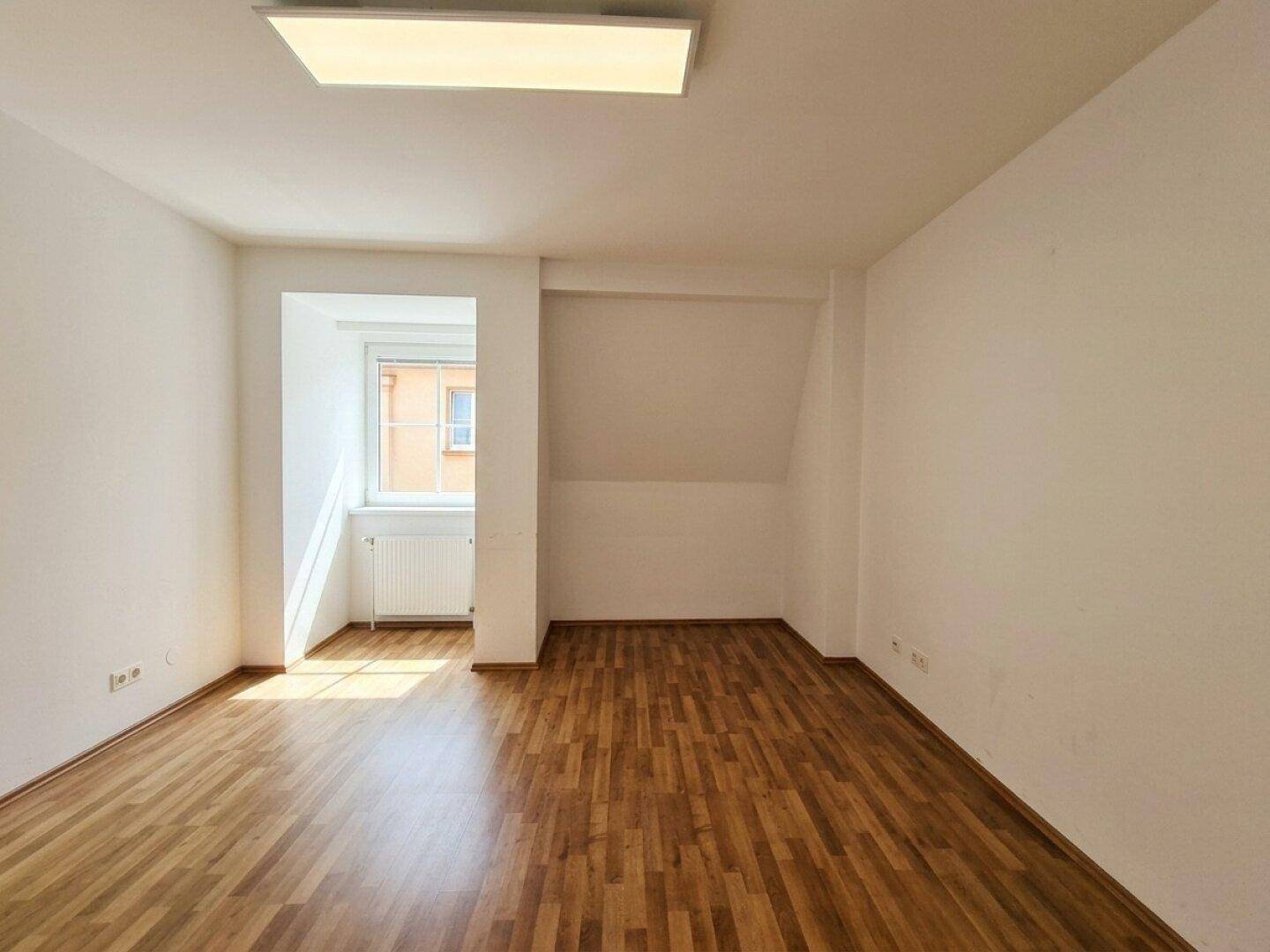Helles Zimmer mit Laminatboden, einem Fenster und Dachschräge, ideal für verschiedene Nutzungen.