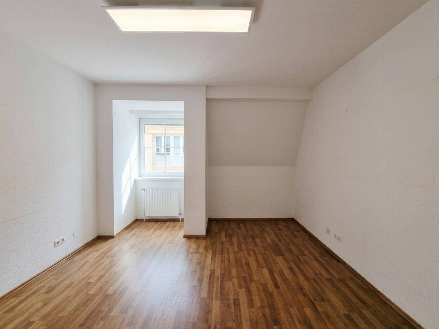 Geräumiges Zimmer mit Laminatboden, einem Fenster und Dachschräge, das viel Tageslicht empfängt.