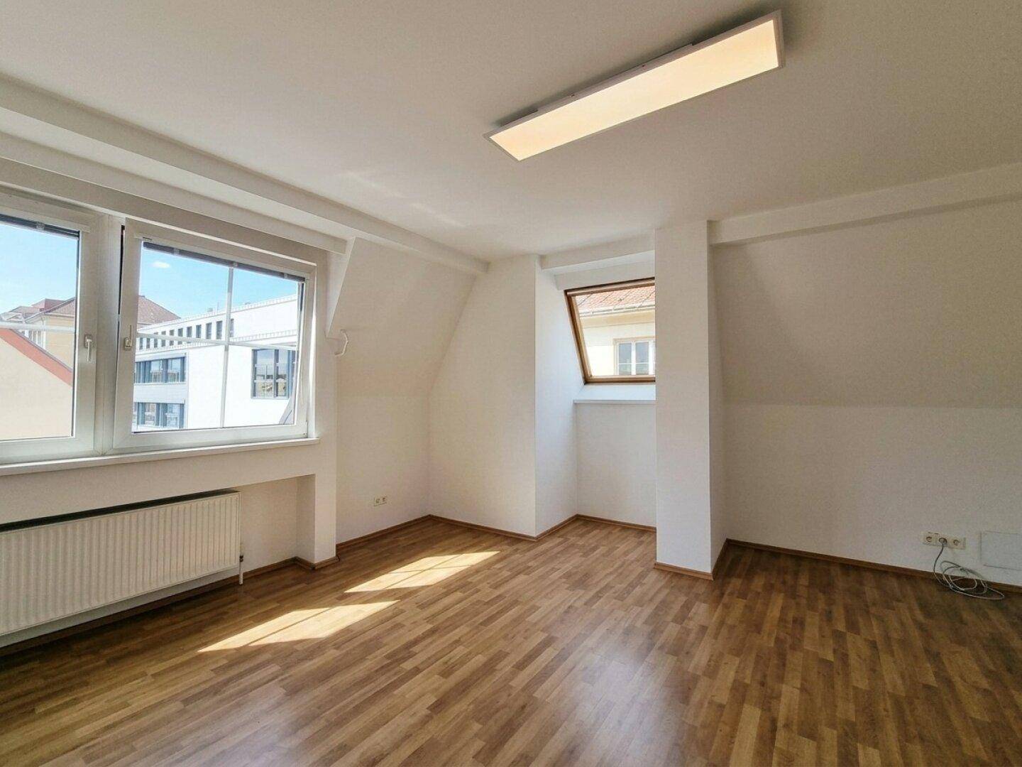 Geräumiges Zimmer mit Laminatboden, zwei Fenstern und Dachschräge, hell und gut gepflegt.