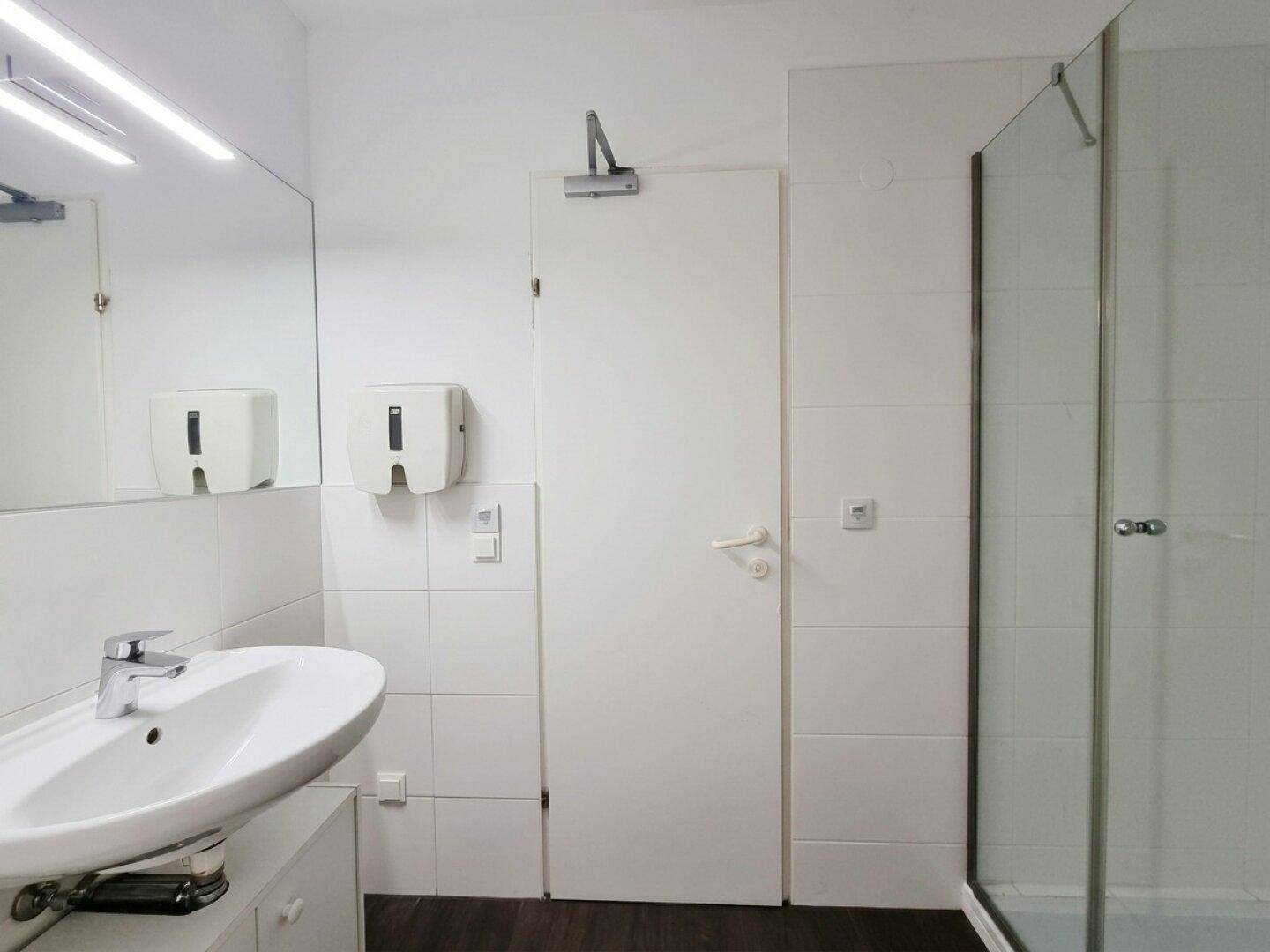 Modernes Badezimmer mit Duschkabine, Waschbecken und weißen Fliesen, gut beleuchtet.