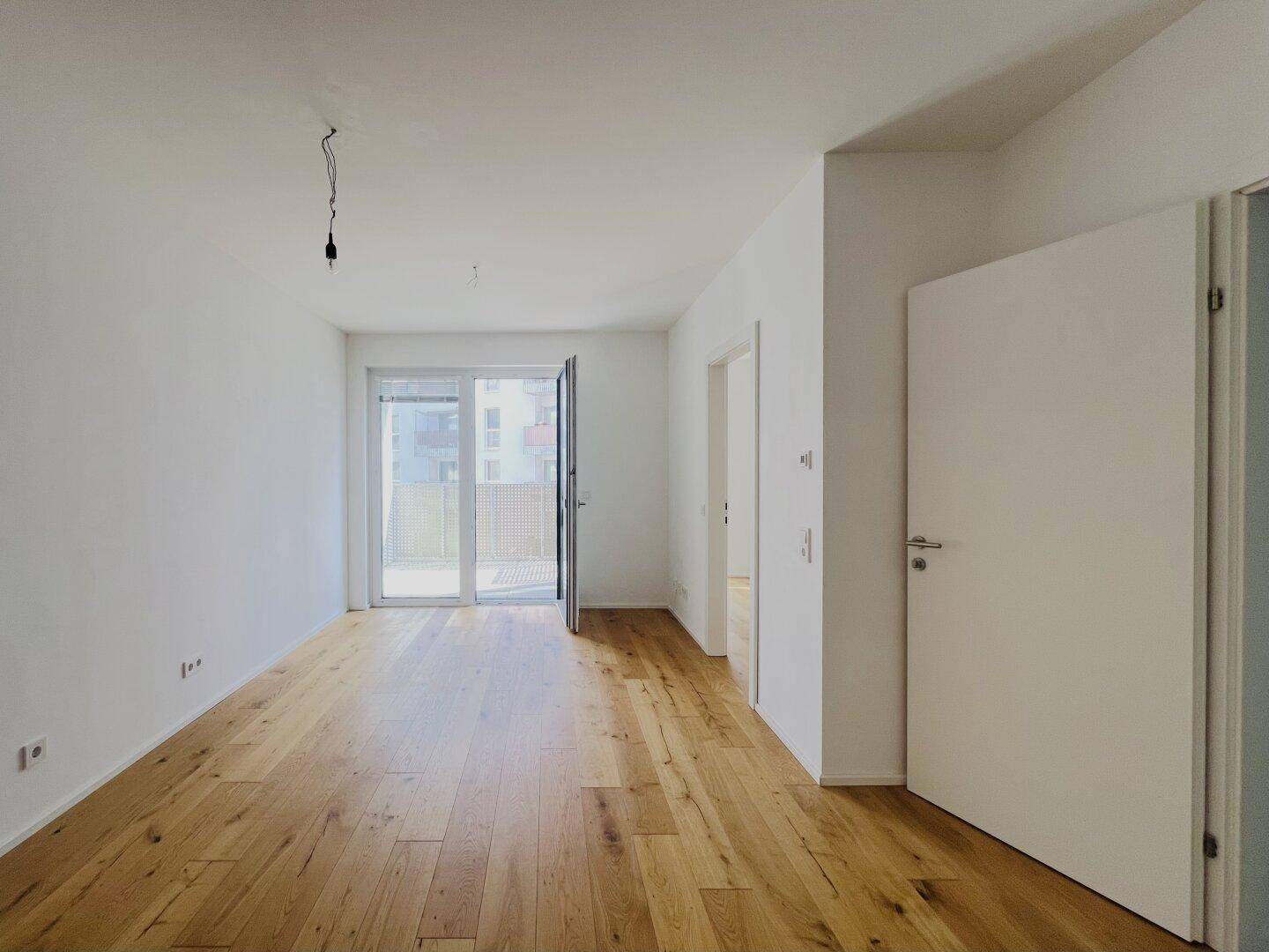 Heller Wohnraum mit Holzboden und großen Fenstern, die viel Tageslicht hereinlassen.