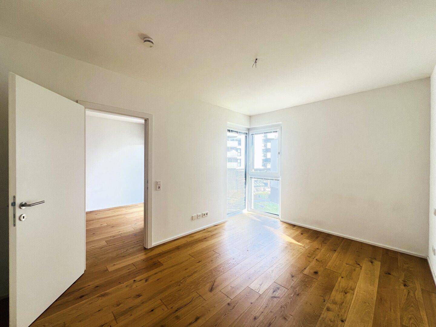 Helles Zimmer mit Holzboden und Zugang zu einem Balkon oder einer Terrasse.