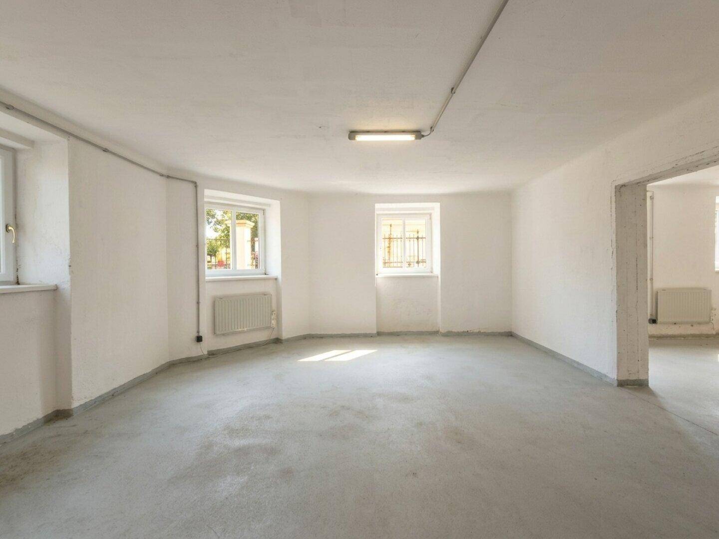 Geräumiger Lagerraum mit Betonboden, weißen Wänden und natürlichem Lichteinfall durch die Fenster.