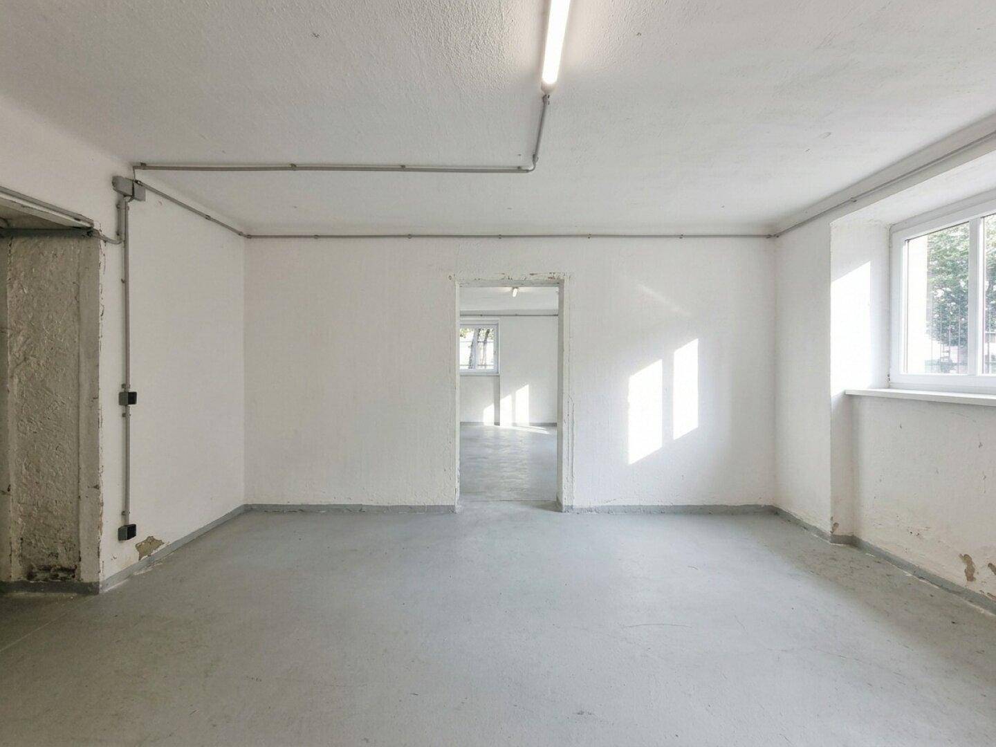 Heller Lagerraum mit Betonboden, einem Fenster und sichtbaren Installationen an den Wänden.