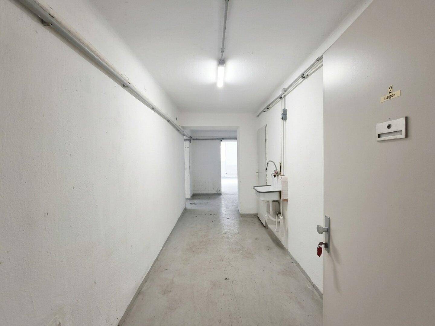 Langer Flur im Kellergeschoss mit Waschbecken und Zugang zu Lagerraum 2.