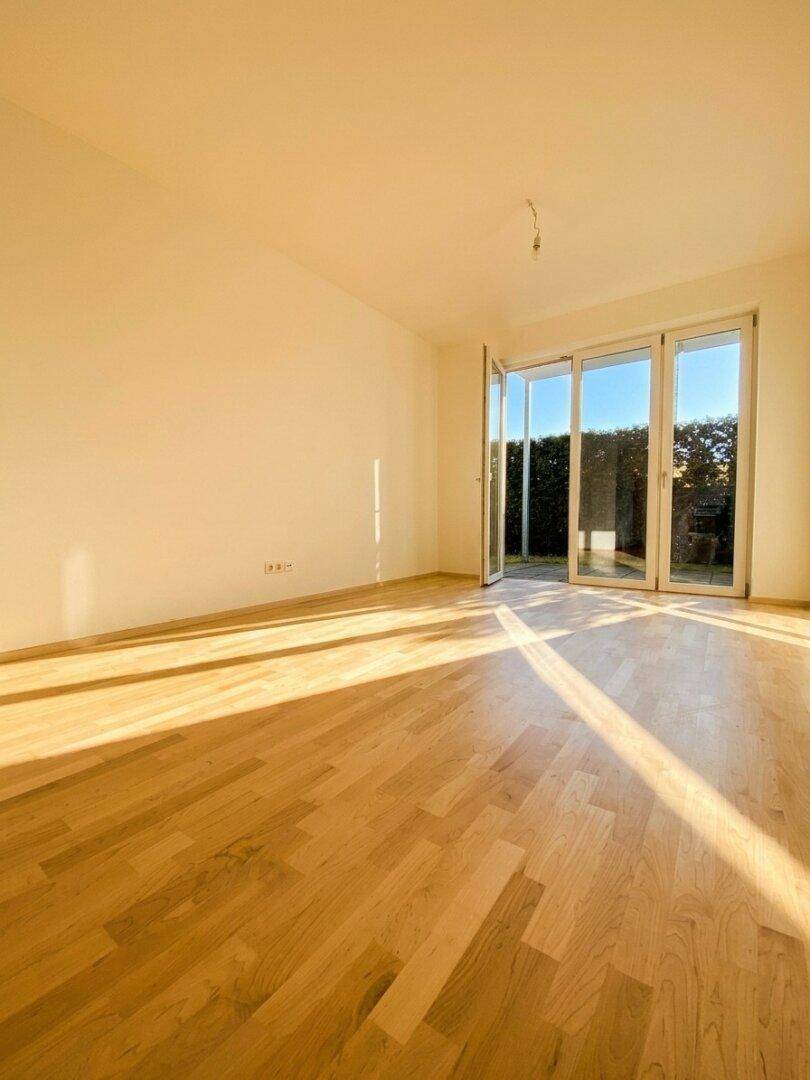 Lichtdurchfluteter Wohnraum mit Holzboden und großen Glastüren, die Zugang zur Terrasse bieten.