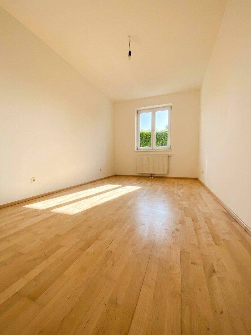 Helles Schlafzimmer mit Parkettboden, großem Fenster und viel natürlichem Lichteinfall.