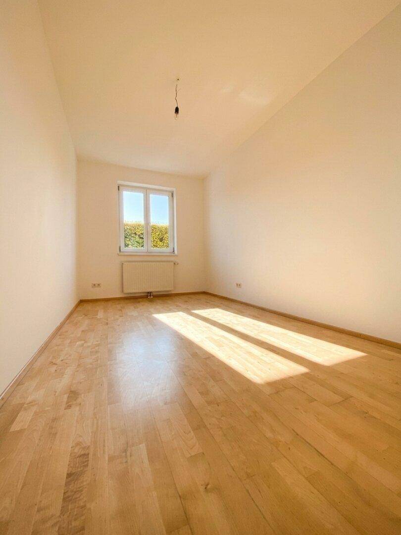 Geräumiges Schlafzimmer mit hellem Parkettboden und einem Fenster, das viel Tageslicht hereinlässt.