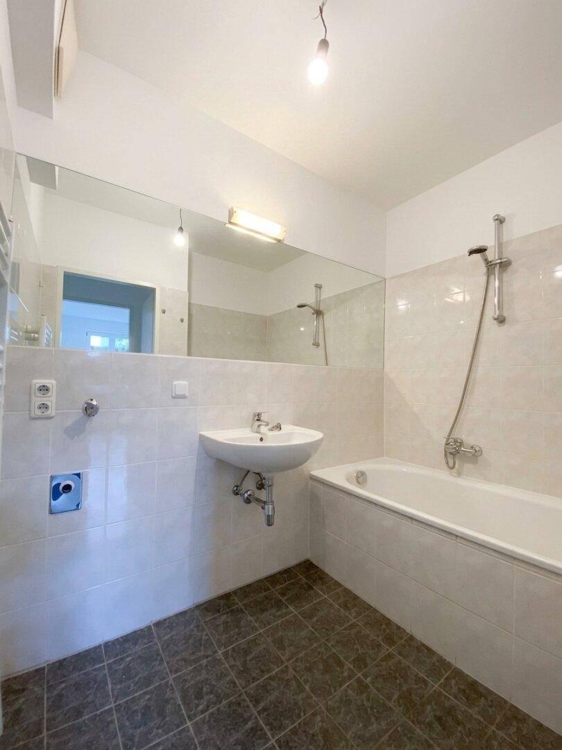 Modernes Badezimmer mit Badewanne, Waschbecken, großem Spiegel und hellen Fliesen.