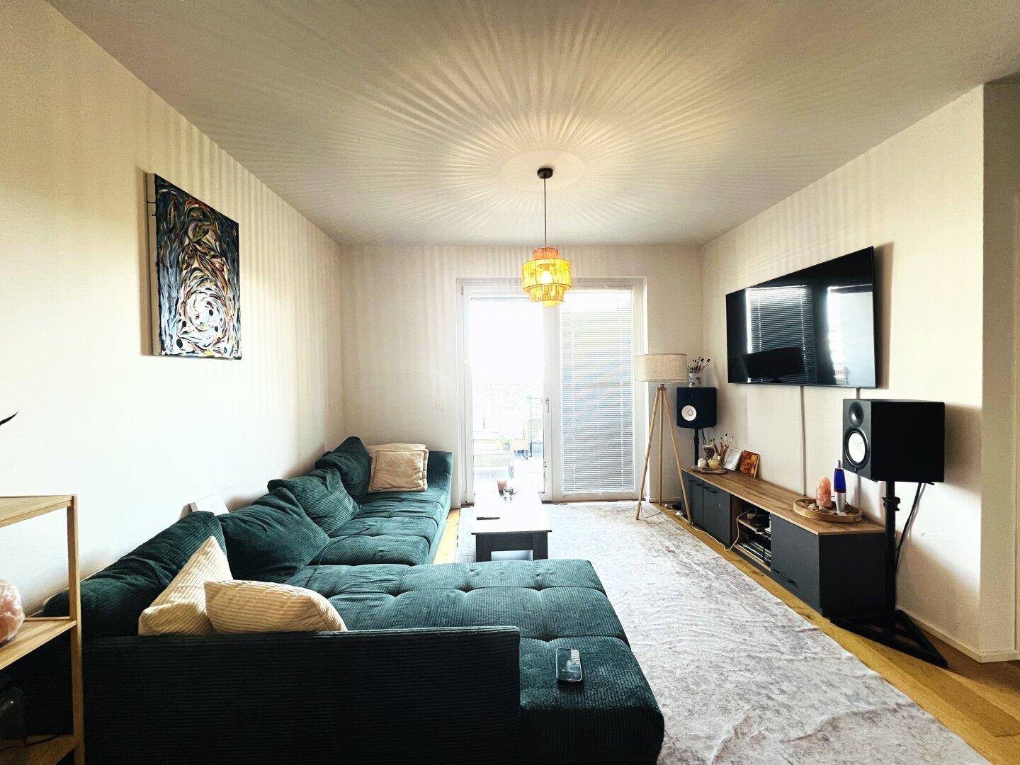 Gemütliches Wohnzimmer mit großer Eckcouch, Fernseher und Zugang zum Balkon.