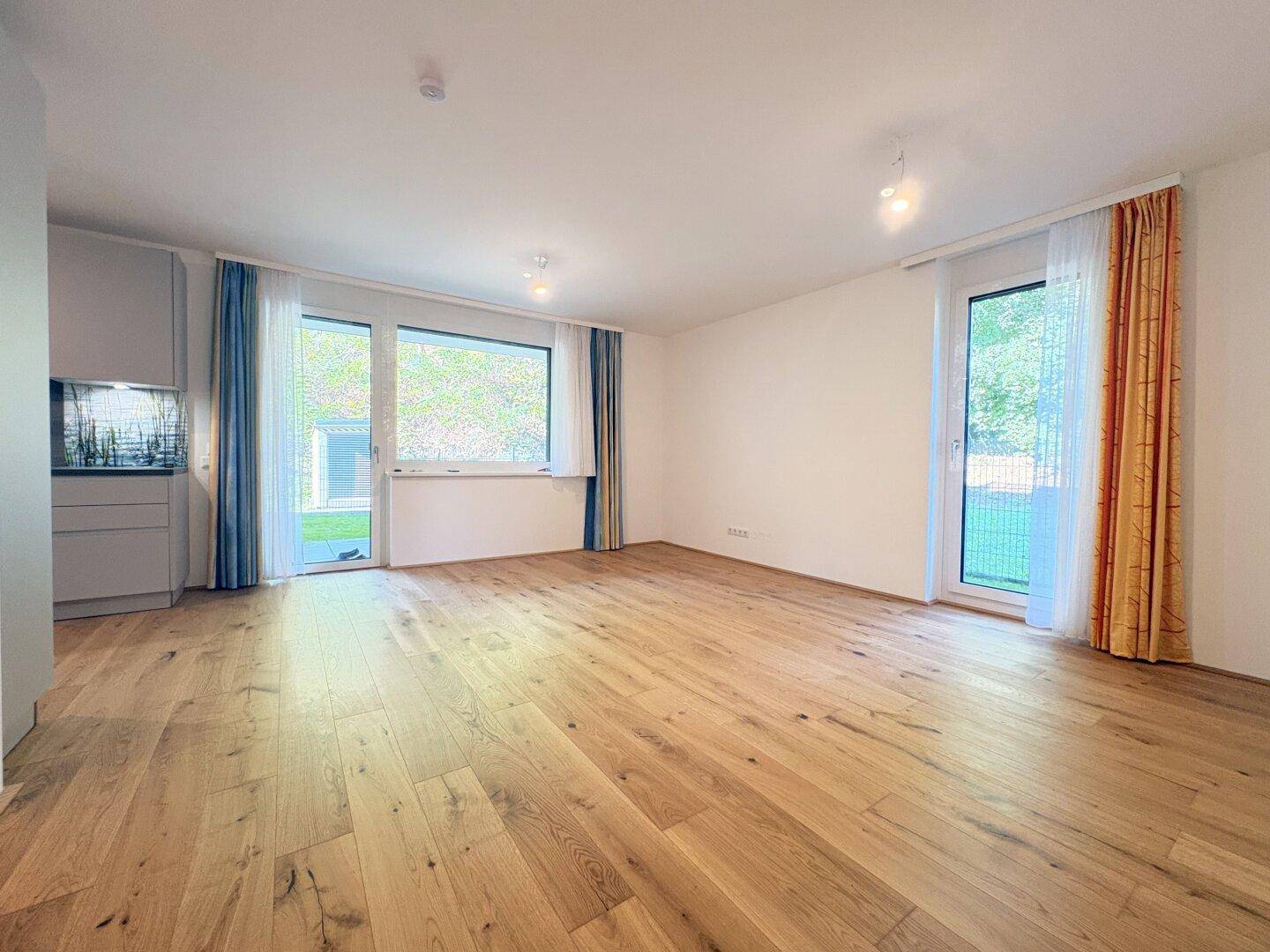 Geräumiges Wohnzimmer mit Holzboden und großen Fenstern zum Außenbereich.